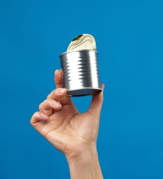 open metal round tin can in a female hand on a blue background, close up