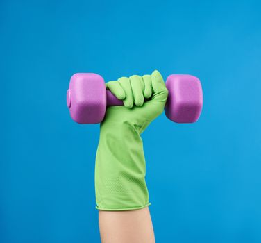 female hand holds a plastic pink dumbbell on a blue background, strong housewife concept