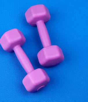 pair of purple plastic dumbbells on a blue neoprene mat, top view, training equipment