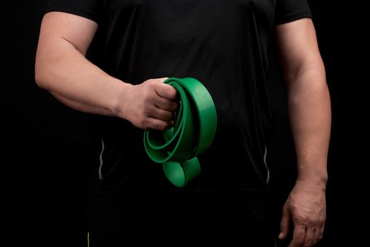 adult athlete with a muscular body in black clothes is doing physical exercises with sport green rubber, low key. Healthy active lifestyle