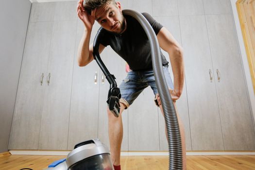 A man with a vacuum cleaner is tired of cleaning the house