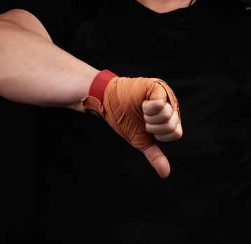 adult athlete in black uniform and hands rewound with textile orange bandage shows gesture dislike, low key