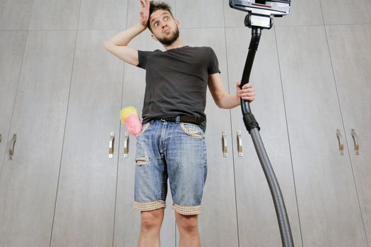 A man with a vacuum cleaner is tired of cleaning the house