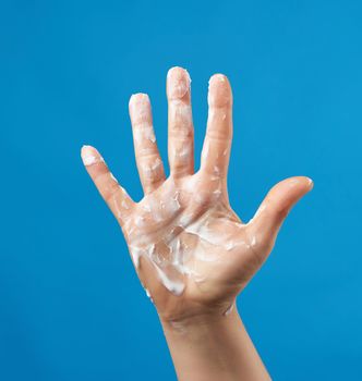 open female palm smeared with white cream on a blue background, moisturizing the skin