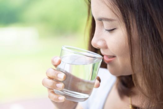 Close up woman drinking pure water from glass with light in the morning, Selective focus