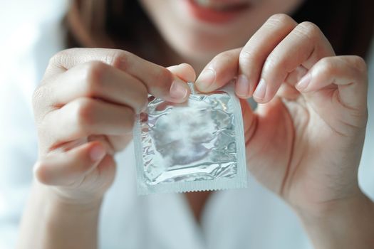 Close up woman hand holding condom lying on white bed, health care and medical concept