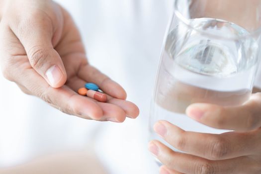 Closeup woman hand holding pills and glass of water, health care and medical concept, selective focus