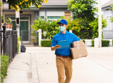 Asian young delivery man courier hold parcel post boxes he protective face mask service and walk looking for customer home location, under curfew pandemic coronavirus COVID-19