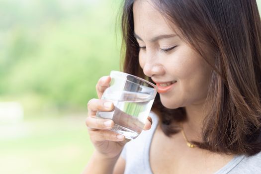 Close up woman drinking pure water from glass with light in the morning, Selective focus