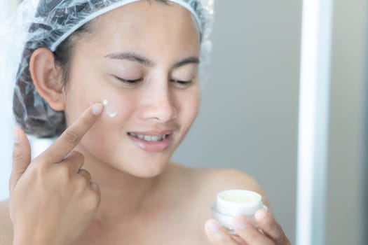 Woman hand applying cream on her face with happy feeling, health care and beauty concept