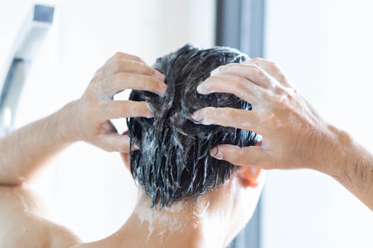 Closeup young man washing hair with with shampoo in the bathroom, vintage tone, selective focus