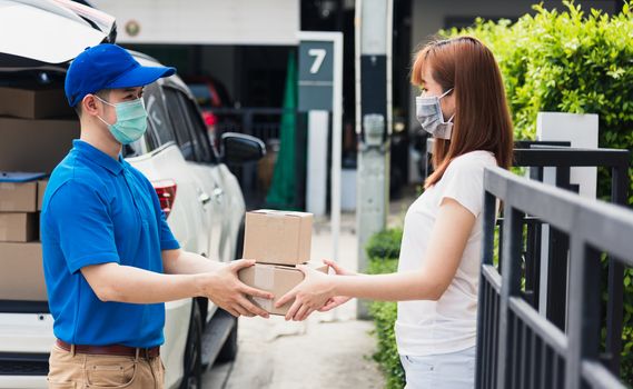 Asian young delivery man courier shopping online give package post box he protective face mask service woman customer receiving box at front home, under curfew quarantine pandemic coronavirus COVID-19