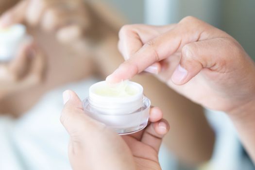 Close up woman hand applying cream or moisturizer from box for face beauty, selective focus