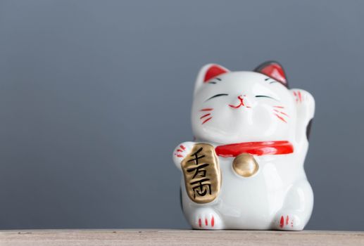 Maneki neko lucky cat show text on hand meaning rich on wood table background, select focus
