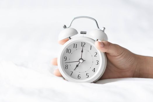 Closeup hand holding alarm clock on white bed, Time to wake up