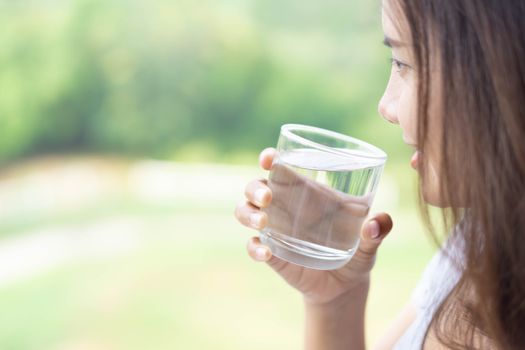 Close up woman drinking pure water from glass with light in the morning, Selective focus