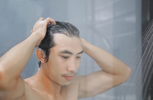 Closeup young man washing hair with with shampoo in the bathroom, vintage tone, selective focus