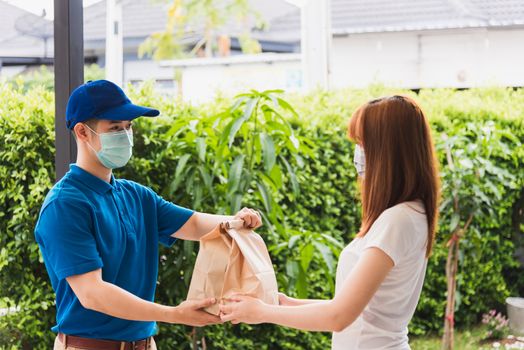 Asian delivery express courier young man giving paper bags fast food to woman customer receiving both protective face mask, under curfew quarantine pandemic coronavirus COVID-19