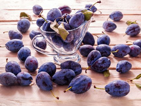 Blue large plums juicy sweet fruit for dietary nutrition lie in a glass goblet on a plank background