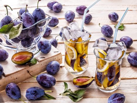 Refreshing drink from fresh juicy sweet sips with lemon in glass mugs with ice cubes on a wooden background with plums and green leaves with plums in a glass sauceboat