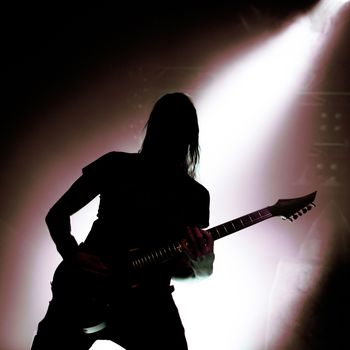silhouette of guitarist with falling light behind, square image