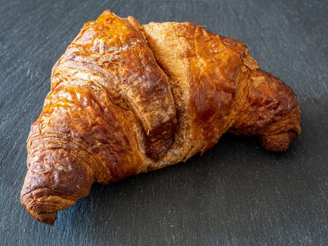 Traditional croissant placed on a dark plate, a typical dessert similar to the Italian Cornetto