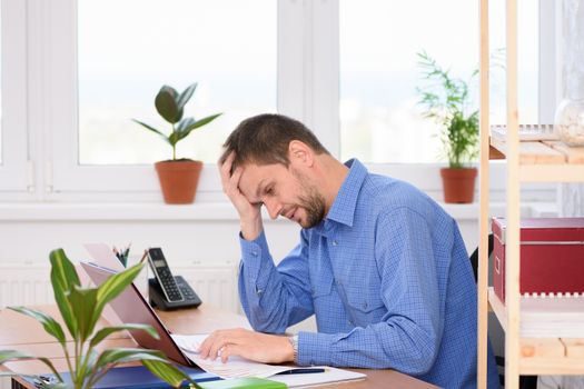 Upset office worker looking at documents clutching his head