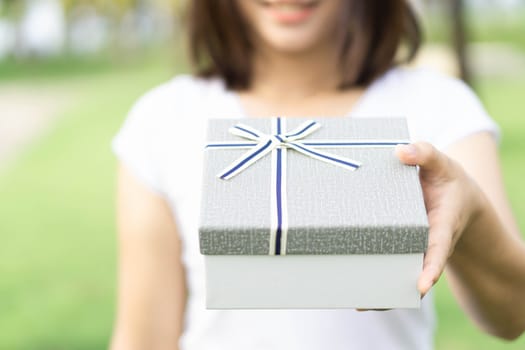 Woman hand holding grey gift box  on green nature background