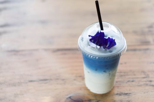 Closeup glass of ice butterfly pea latte on wood table with nature background