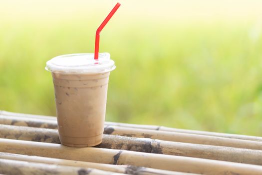 Close up glass of ice cappuccino coffee on wood table with green nature background, selective focus