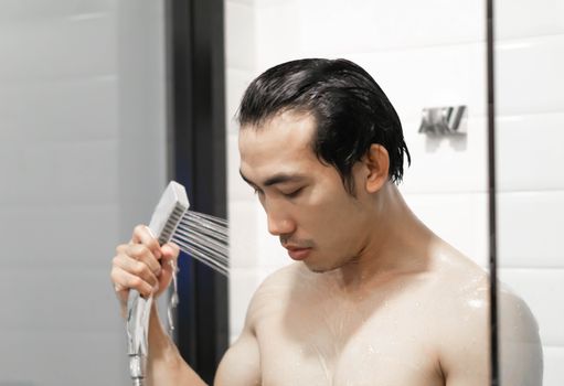 Closeup handsome asian man taking a shower in the bathroom, selective focus