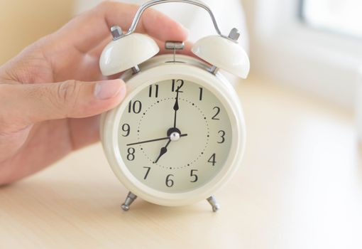 Closeup hand holding alarm clock on table in bedroom, Time to wake up