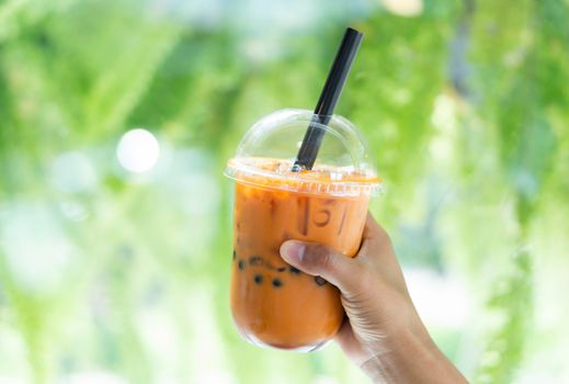 Closeup hand holding glass of ice thai tea with nature background