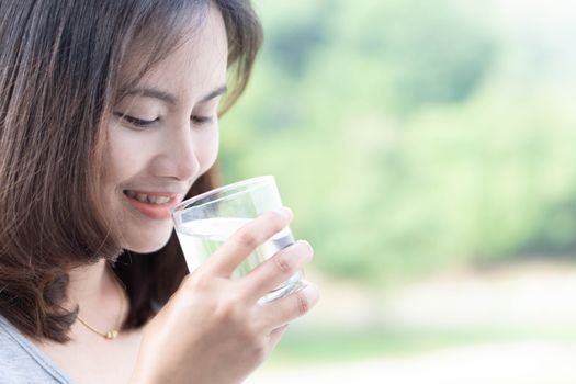 Close up woman drinking pure water from glass with light in the morning, Selective focus