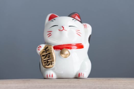 Maneki neko lucky cat show text on hand meaning rich on wood table background, select focus