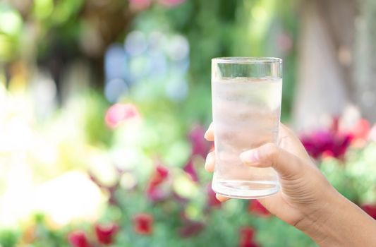 Close up woman hand holding a glass of pure water for dink with green nature background, Health care concept