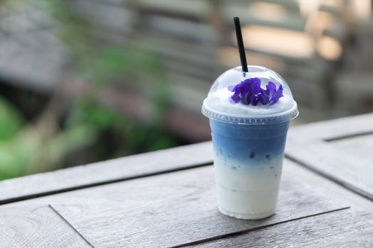 Closeup glass of ice butterfly pea latte on wood table with nature background