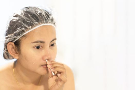 Close up woman looking her face in the mirror with cotton brush cleaning nose after bath, health care and beauty