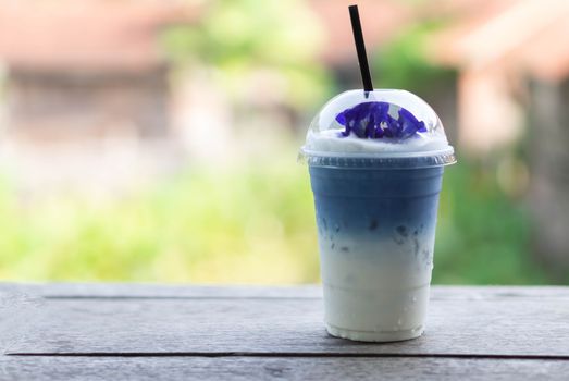 Closeup glass of ice butterfly pea latte on wood table with nature background