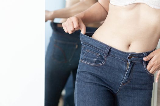 Woman showing jeans pants and body after weight loss and sexy body with mirror and white wallpaper background