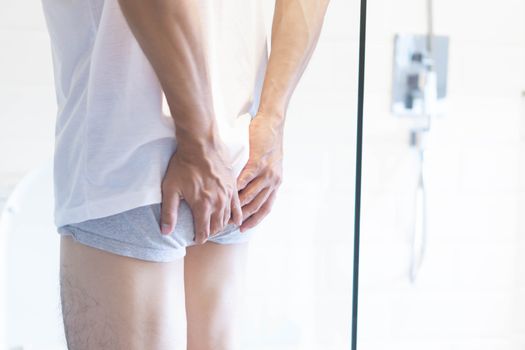 Closeup man holding bladder with pee pain in the toilet, selective focus