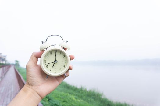 Alarm clock in hand with nature and fog background in the morning