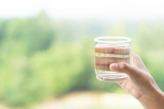 Close up woman hand holding a glass of pure water for dink with green nature background, Health care concept