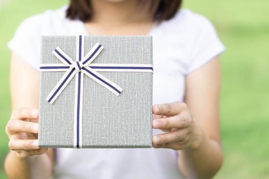 Woman hand holding grey gift box  on green nature background