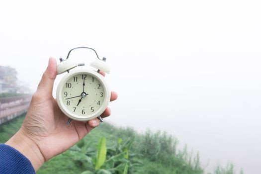 Alarm clock in hand with nature and fog background in the morning