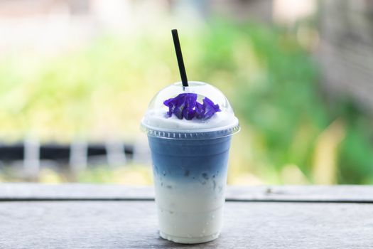 Closeup glass of ice butterfly pea latte on wood table with nature background