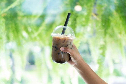 Closeup hand holding glass of ice coffee with bubble milk nature background