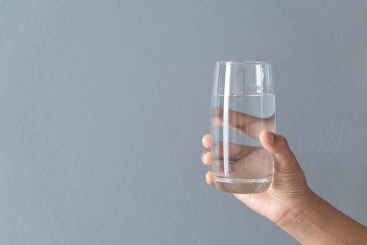 Close up woman hand holding a glass of pure water for dink with grey background, Health care concept