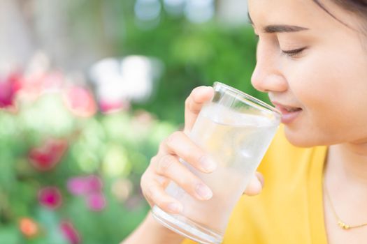 Close up woman drinking pure water from glass with light in the morning, Selective focus