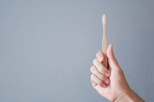 Closeup man hand holding wooden toothbrush with grey background, health care concept